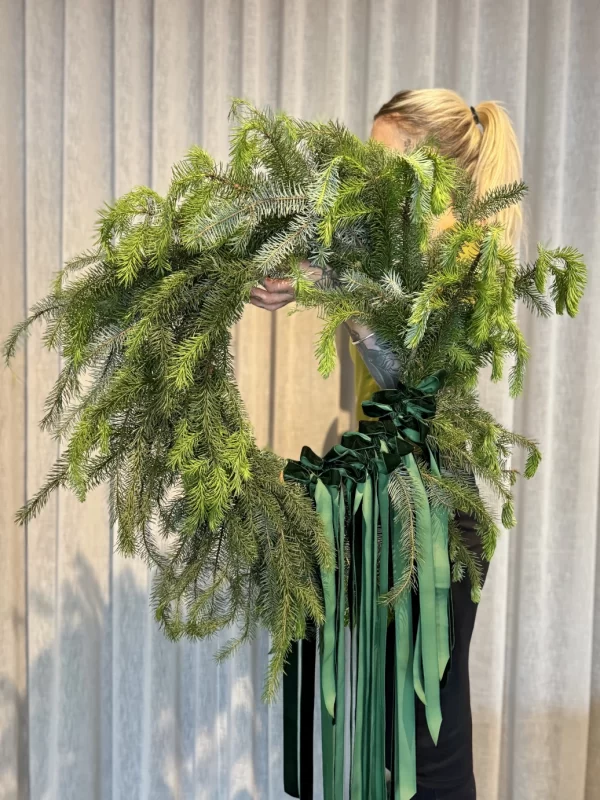 Woman holding a green wreath decorated with green ribbon and bows.